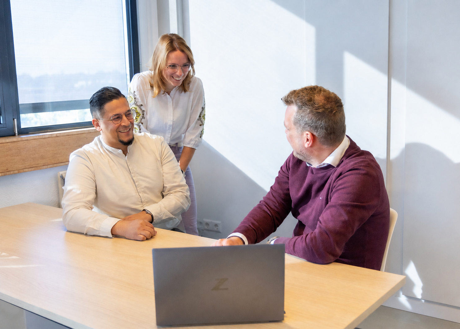 Three colleagues in discussion at a meeting table with a laptop